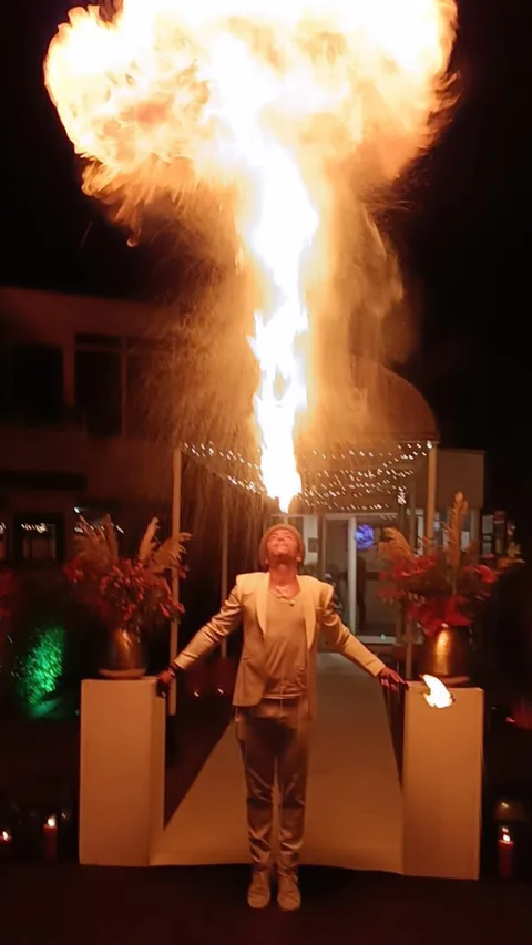 In wit gala-kostuum blaast Nuno een metershoge vuurzuil tussen bloemen en kaarsen op een chique feest