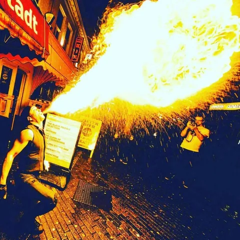 Vuurspuwer Nuno blaast een enorme vuurzee met vonkenregen in een uitgaansstraat bij nacht
