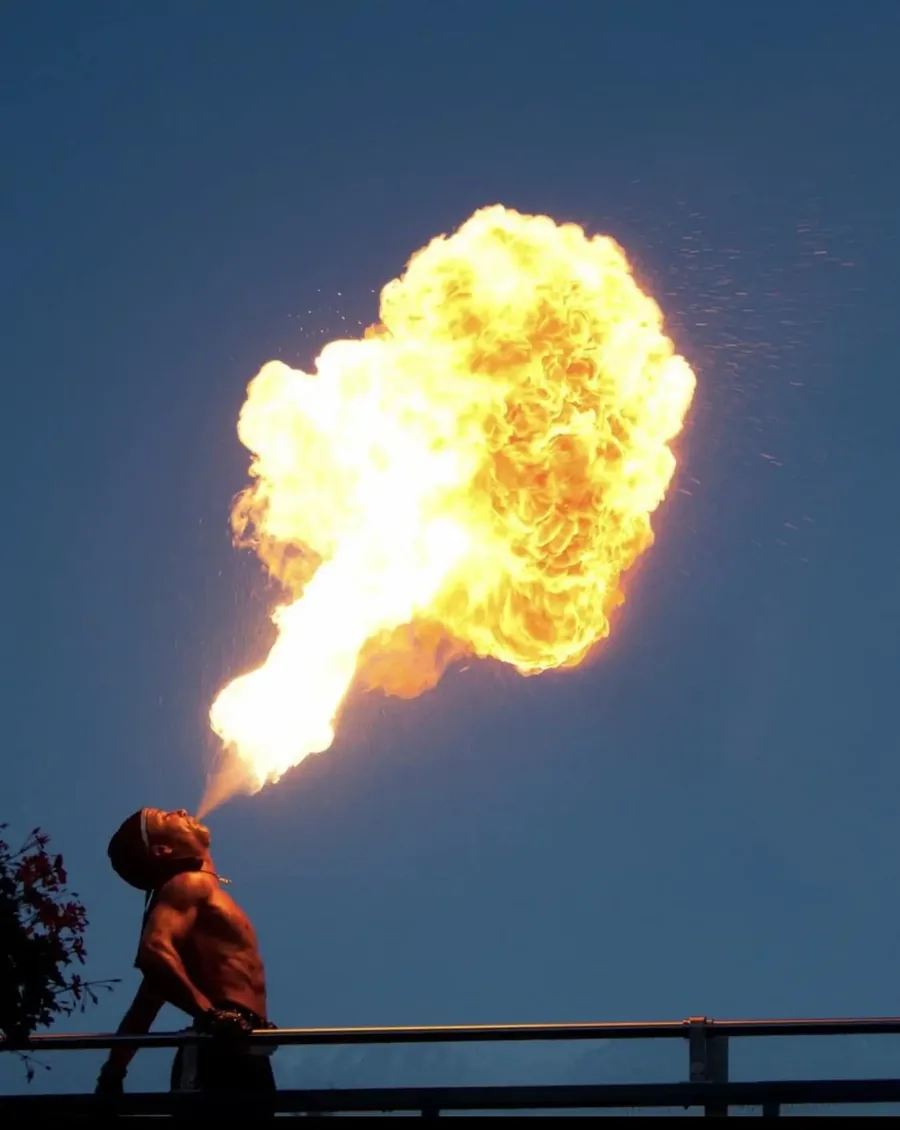 Vuurspuwer blaast een grote vuurbal tegen de avondlucht tijdens de workshop vuurspuwen